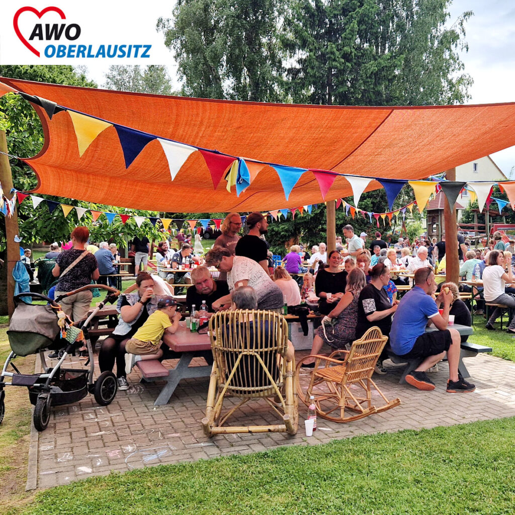 Sehr viele Besucher sitzen auf Bänken. Dabei essen und trinken sie.