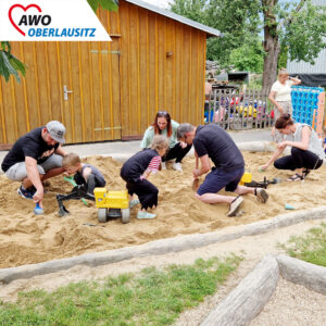Erwachsene und Kinder graben zusammen im Sandkasten.