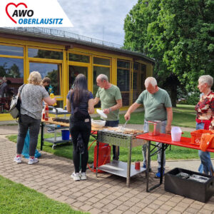 Zwei Männer sind am grillen, während sich andere die Bratwürste nehmen und essen.