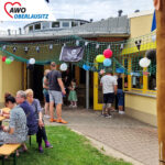 Besucher betreten das Gebäude. Andere sitzen draußen auf Bänken.