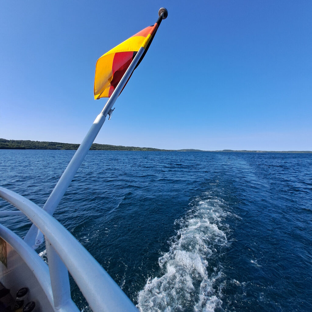 Blick vom Boot auf den See. Am Mast ist eine Deutschlandflagge gehisst.