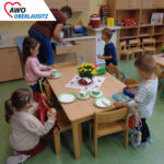 vier Kinder decken mit Hilfe der Erzieherin den Tisch