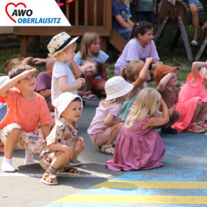 viele Kinder sitzen in der Hocke und halten sich die Hand an die Stirn um sich vor der Sonne zu schützen