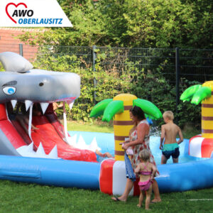 Kinder baden und spielen in einem großen Pool. Der Pool hat eine Rutsche, die die Zunge von einem Hai ist.
