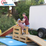 Ein Mann hilft den Kinder auf die Rutsche hinauf zu kommen
