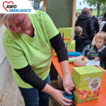 Frau zapft Apfelsaft für ein Kind in einen Becher am Stand eines Kinderfestes.