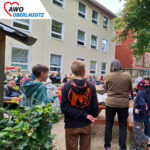 Viele Eltern und Kinder zu Besuch beim Fest. Sie essen Kuchen, basteln an den Ständen, sitzen gemeinsam an Tischen.