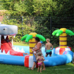 Kinder baden und spielen in einem großen Pool. Der Pool hat eine Rutsche, die die Zunge von einem Hai ist.