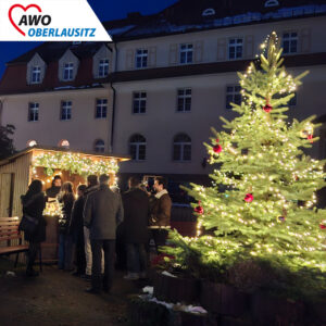 Weihnachtlich geschmückte Holzbuden neben einem leuchtenden Weihnachtsbaum vor dem Gebäude des Olbersdorfer Altenheims.