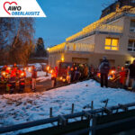Vor dem weihnachtlich geschmückten Altenheim stehen aufgereiht Freiwillige Feuerwehr sowie junge und alte Besucher des Lichterfestes mit Fackeln in den Händen. Gleich soll der Fackelumzug starten.