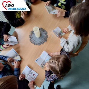 Die Perspektive von oben zeigt eine Tischplanne. Um den Tisch sitzen Kinder. Alle schauen nach unten und blättern in einem Pixibuch.