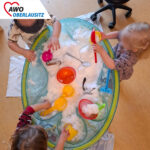 Drei Krippenkinder spielen im Gruppenzimmer mit den Sandförmchen in einer Wanne mit frischem Schnee.