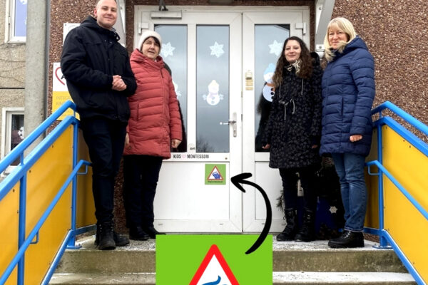 Vor dem Haupteingang der Kita "Bergblick" stehen Kitaleiter Herr Freytag und Kolleginnen vom Deutschen Kinderschutzbund (Ortsgruppe Zittau). An der Tür ist der bekannte Aufkleber der "Elefantenstark!!-Initiative zu sehen. Ein kleiner Elefant in einem roten Dreieck auf hellgrünem Untergrund.