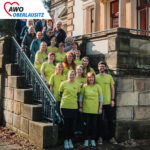 Das Team der Kita "Knirpsenland" steht in grünen Teamshirts mit Frau Dähne-Bartsch auf der Eingangstreppe.