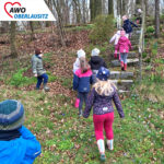 Viele Kinder, mit Jacken und Mützen, stürmen im Wald eine Steintreppe hinauf auf der Suche nach Osternestern.